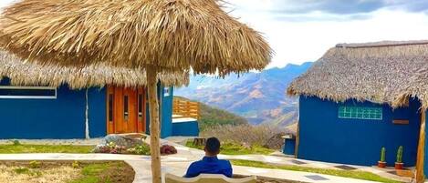 A person sitting under a thatched roof structure in a courtyard with a mountain view.