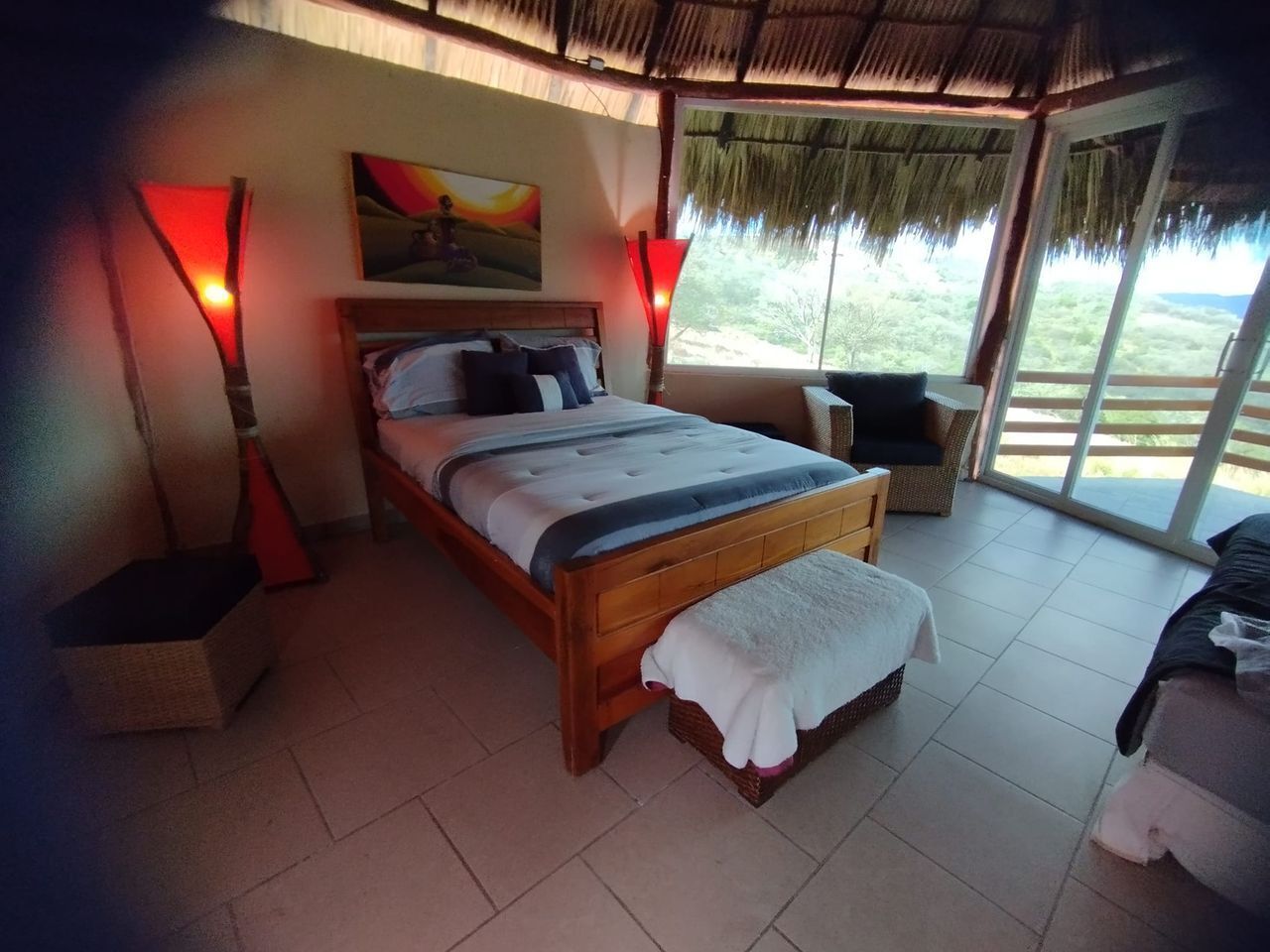A bedroom with a bed, bedside tables, a window, and a view of the outdoors.