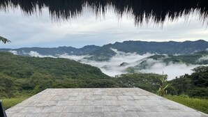 A stone-tiled patio with a view of lush green hills and a misty valley.