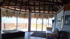Una habitación con techo de paja, ventanas amplias, un sofá, una silla y una bañera.
