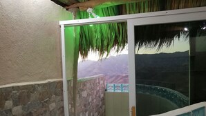 Un balcón con pared de piedra, puerta de cristal y vista a un puente y montañas.