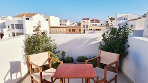 Terraza en la azotea con mesa y sillas de madera, rodeada de muros blancos y follaje.