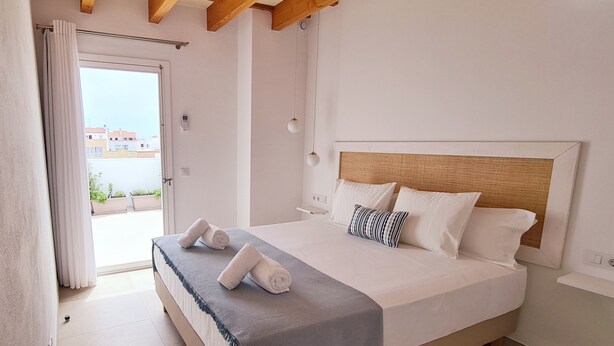 Un dormitorio con cama, techo de madera, ventana con cortinas y vistas a edificios.