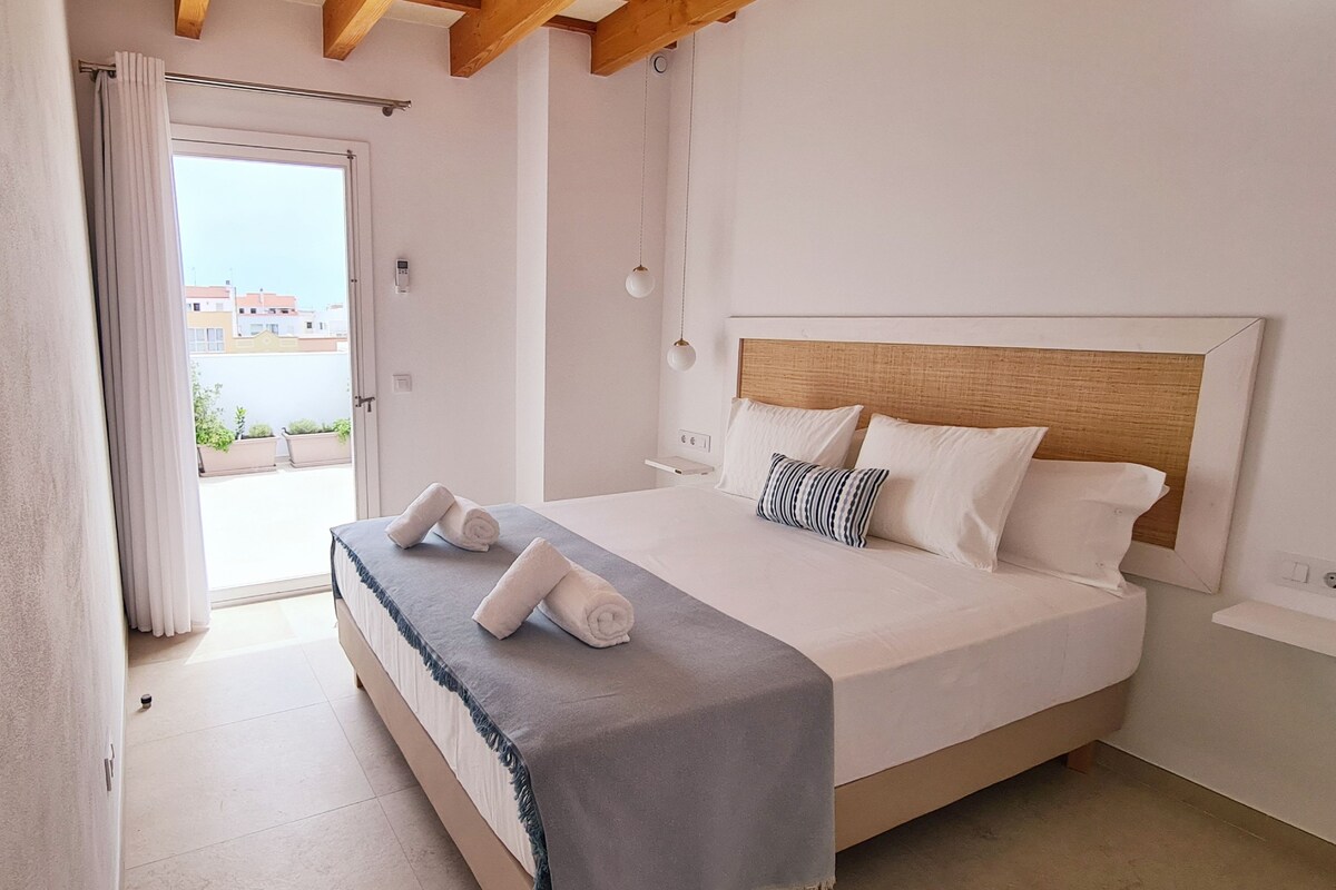 Un dormitorio con una cama, techo de madera, una ventana y vistas a edificios.