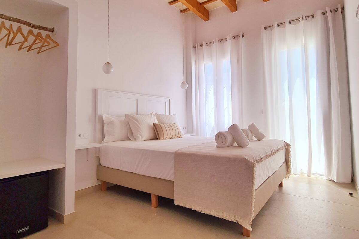 Un dormitorio con cama, vigas de madera, una lámpara colgante y una ventana con cortinas.