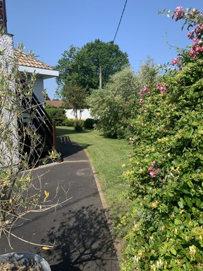 Une rue résidentielle avec un chemin pavé, une végétation luxuriante et une maison dont le toit est recouvert de tuiles.