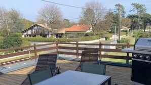 An outdoor patio with a table and chairs, a grill, and a view of houses and trees. - Loft 1er Étage (Andernos-les-Bains)