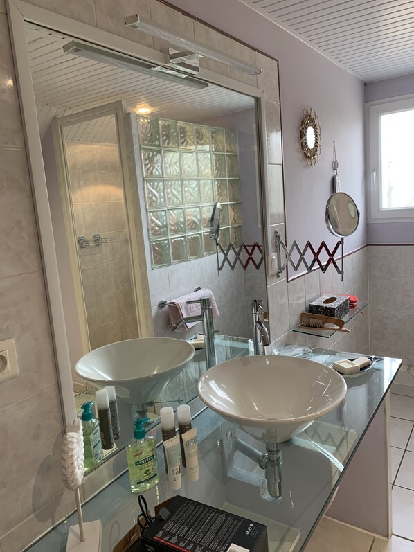 Een moderne badkamer met twee grote glazen wastafels, een grote spiegel en een douche met glazen deur.