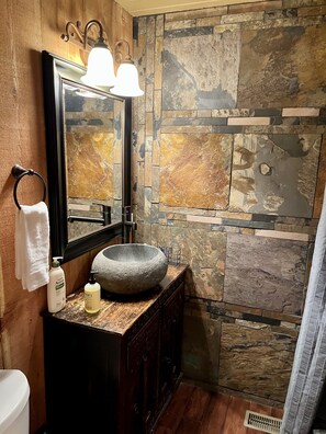 Un baño con lavabo de piedra, tocador de madera y un espejo grande con iluminación.