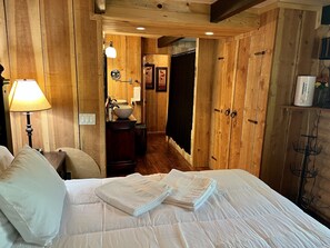 Una habitación de madera con cama, mesita de noche, lámpara, lavamanos y espejo.