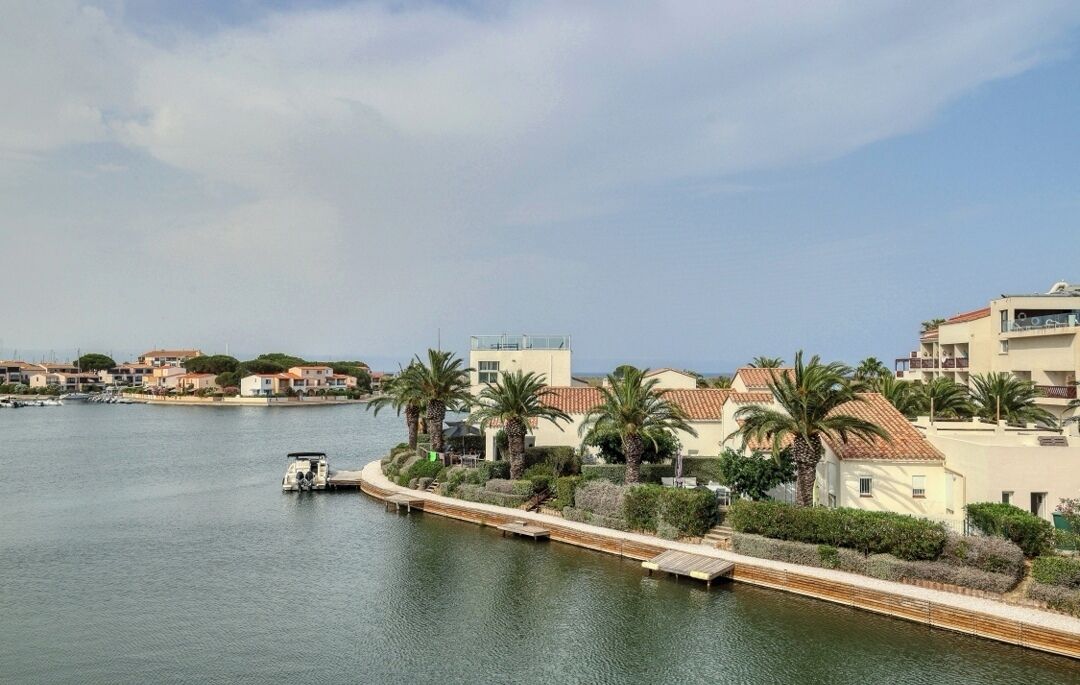 A waterfront property with a dock, palm trees, and buildings with red-tiled roofs.