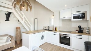 Uma cozinha moderna com armários brancos, máquina de lavar embutida, micro-ondas e máquina de café.