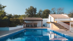 Une piscine avec une terrasse carrelée, un espace extérieur couvert aménagé en salon et un escalier menant à un deuxième niveau.