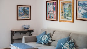 Un salon avec un canapé, une petite table sur laquelle se trouve un bol, et trois œuvres d’art encadrées accrochées au mur.