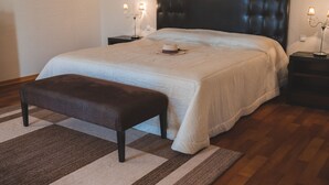 Une chambre à coucher avec un grand lit, un banc, deux tables de chevet avec des lampes et un plancher en bois.