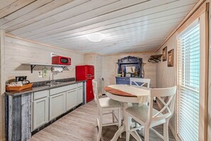 Una cocina compacta con armarios blancos, un refrigerador rojo, una zona de bar azul y una mesa de comedor con sillas.