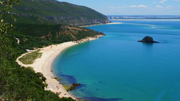 Eine Küstenlandschaft mit Strand, klarem blauen Wasser und einem Bergpanorama im Hintergrund.