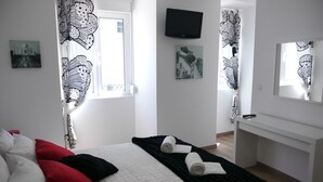 Ein Schlafzimmer mit Bett, Kissen, Fernseher, Kunstwerken und einem Schreibtisch.
