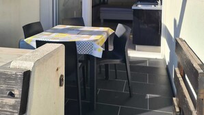 Pihalla on terassi, jossa on pöytä ja tuoleja, pieni keittiö, jossa on pesuallas, ja liukuovi, joka johtaa sisätiloihin.
