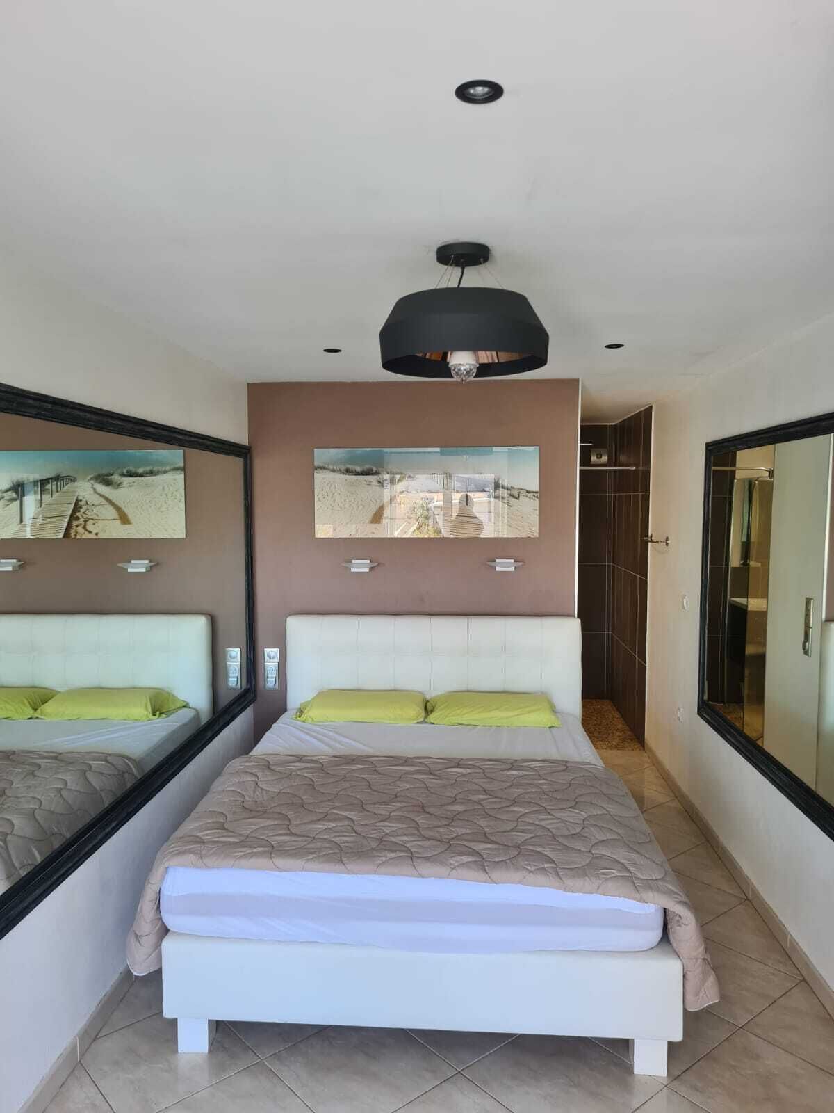 A bedroom with a large bed, two bedside tables, a mirror, and a ceiling light.