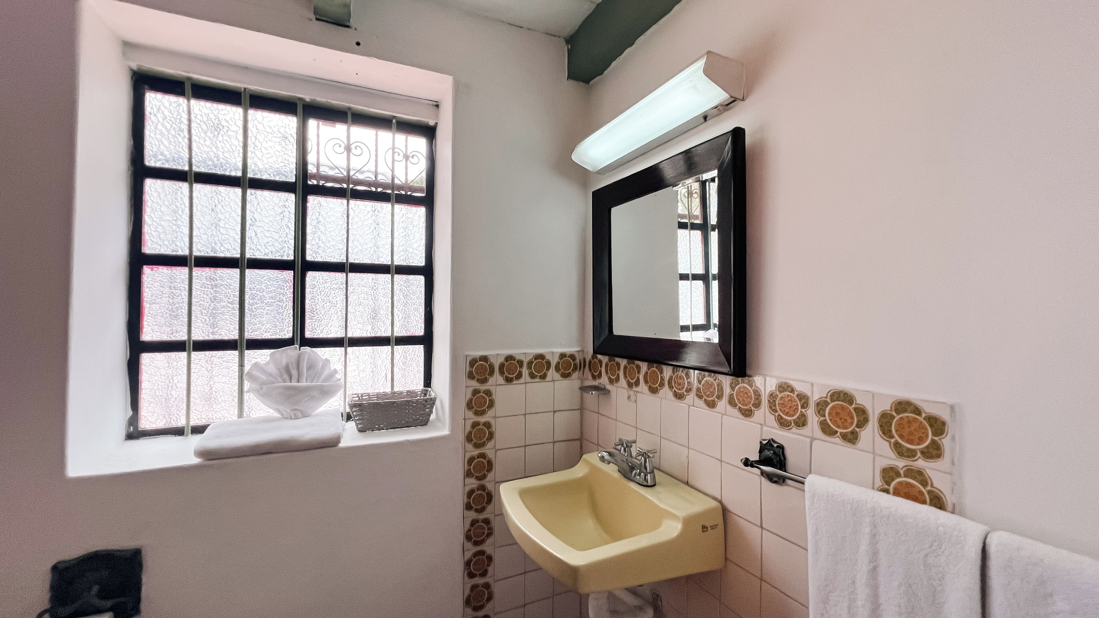 Een badkamer met een raam, wastafel, spiegel en handdoekhouder.