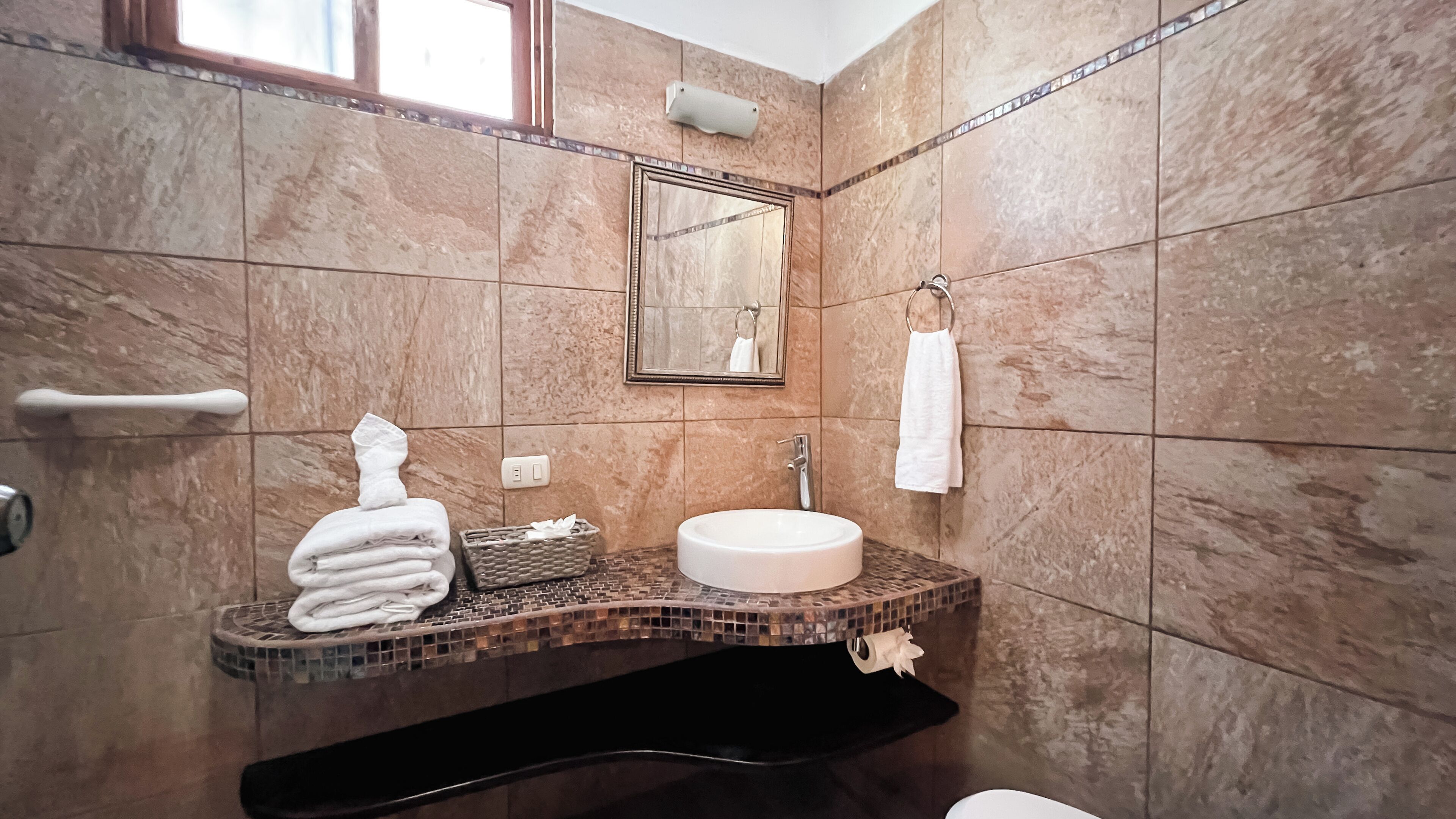 A bathroom with a marble-tiled wall, a sink, a mirror, and a towel rack.