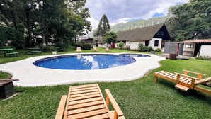 A swimming pool with a wooden deck, surrounded by grass and trees. - Hotel Rancho Grande (Panajachel)