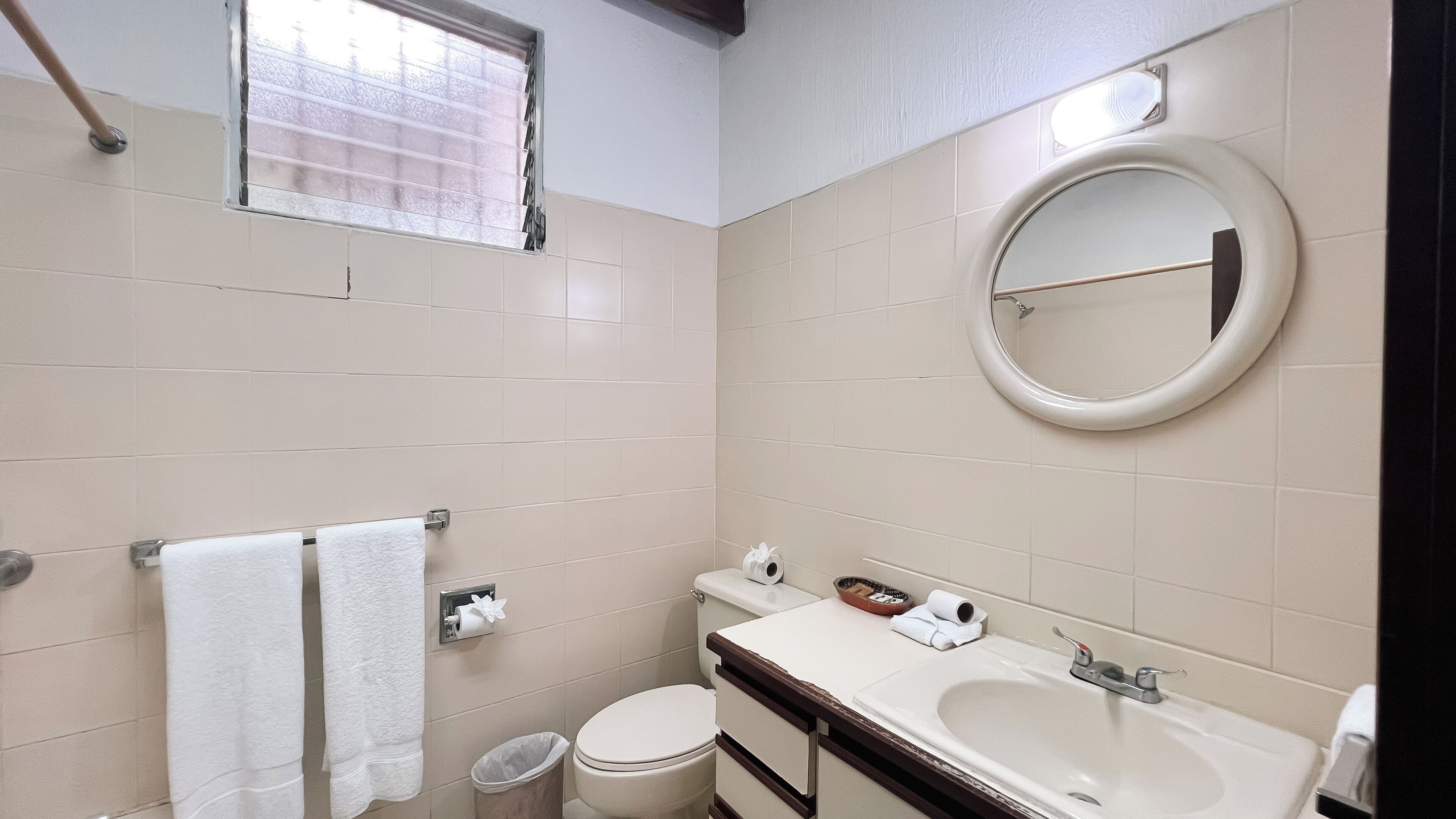 A bathroom with a toilet, sink, mirror, towel rack, and a window with blinds.