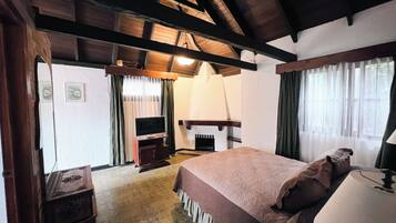 A bedroom with a bed, a television, a fireplace, and a window with curtains.