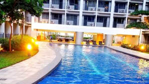 A swimming pool with a tiled edge, surrounded by a building with multiple balconies and air conditioning units. - Deluxe Suit Room (Pasay)