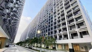 A modern high-rise building with a grid of balconies, a wide pedestrian walkway, and a clear sky. - Deluxe Suit Room (Pasay)