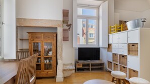 A cozy room with a wooden dining table, two stools, a cabinet with glass doors, a television, and a window with a view of buildings. - Fully new refurbished Alfama Central Cosy Home (Lisboa)