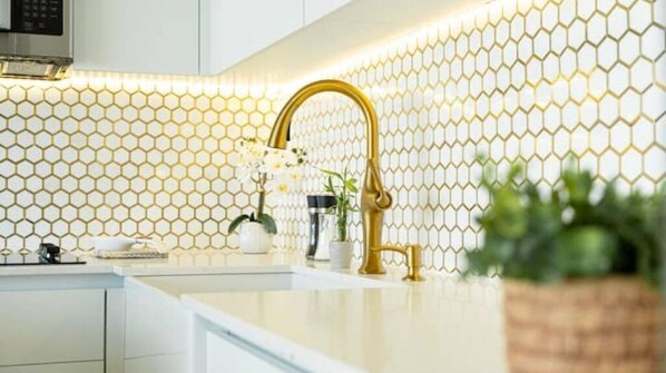 A modern kitchen with a honeycomb-patterned backsplash, a gold faucet, and a potted orchid.