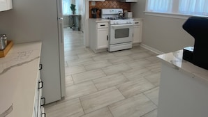 Uma cozinha moderna com armários brancos, uma geladeira branca, micro-ondas, fogão e pia.