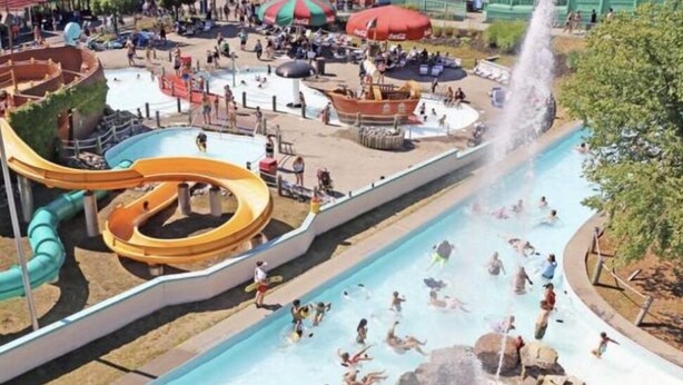 Parque acuático con múltiples toboganes y piscinas, rodeado por una zona vallada con asientos y sombrillas.
