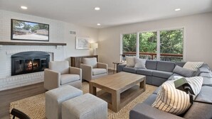 Un salon moderne doté d’une cheminée, de sièges confortables et de grandes fenêtres offrant une vue sur l’extérieur.