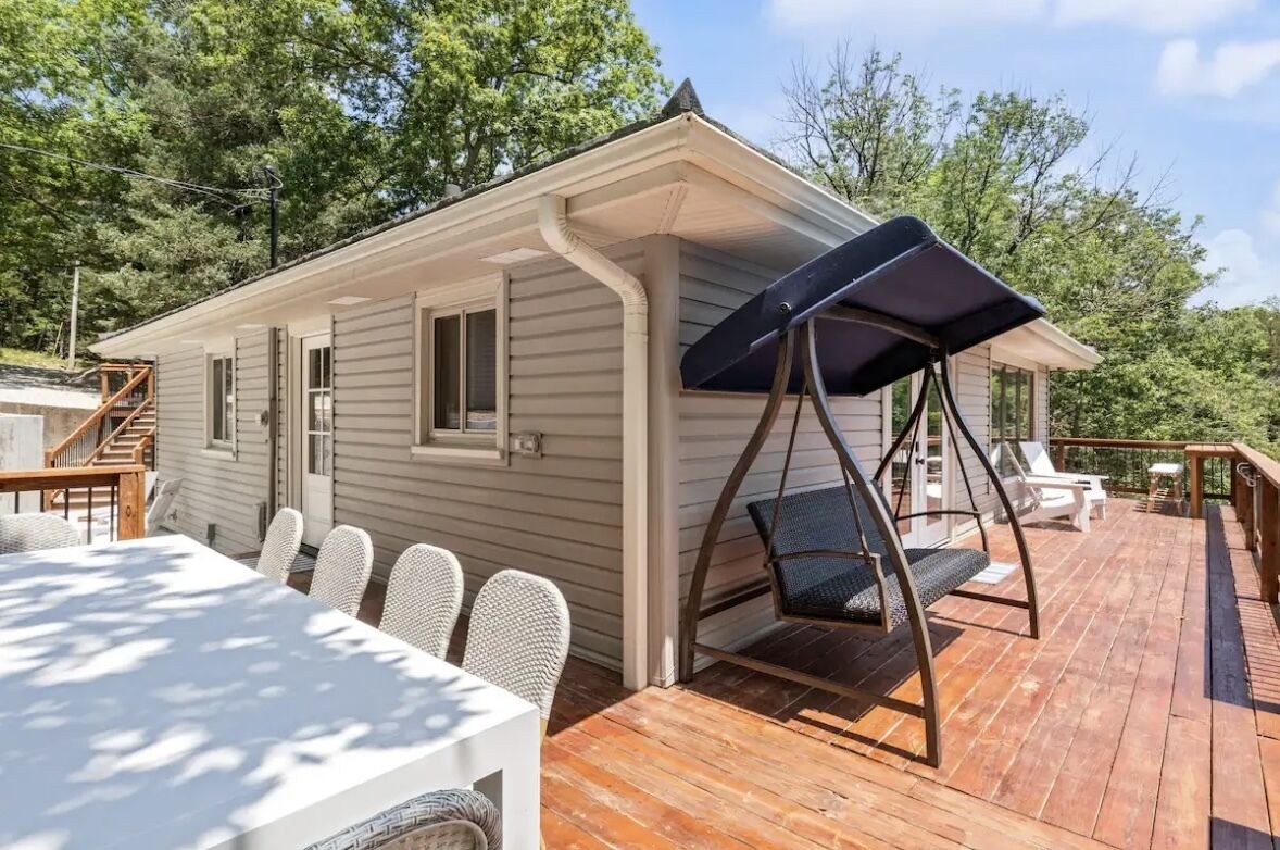A wooden deck with a dining table and chairs, a swing chair, and a covered seating area.