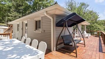 A wooden deck with a dining table and chairs, a swing chair, and a covered seating area.