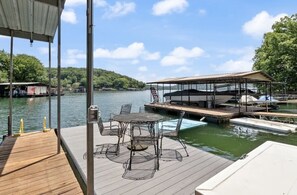 A wooden dock with a covered seating area and a table with chairs, overlooking a calm lake with boats and a docked yacht. - Waterfront House with Private Dock (Rocky Mount)