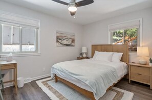 A bedroom with a bed, bedside tables, a ceiling fan, a window with blinds, and a painting on the wall. - Waterfront House with Private Dock (Rocky Mount)
