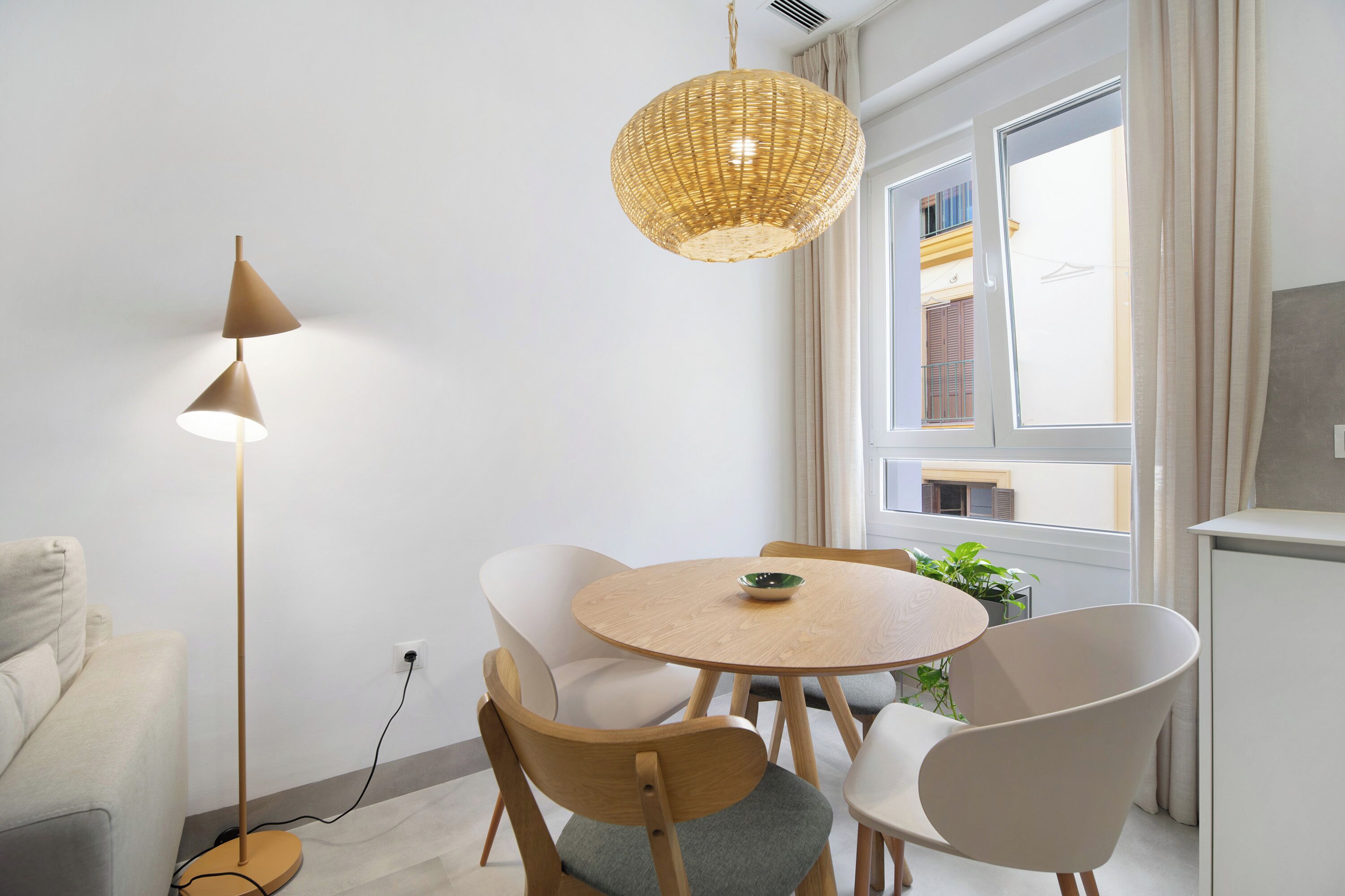 A modern living room with a round wooden table, white chairs, a floor lamp, and a hanging light fixture.