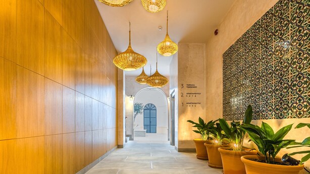 Un couloir aux murs lambrés, orné de lustres en osier suspendus, de plantes en pot et d’un mur carrelé présentant un motif géométrique.