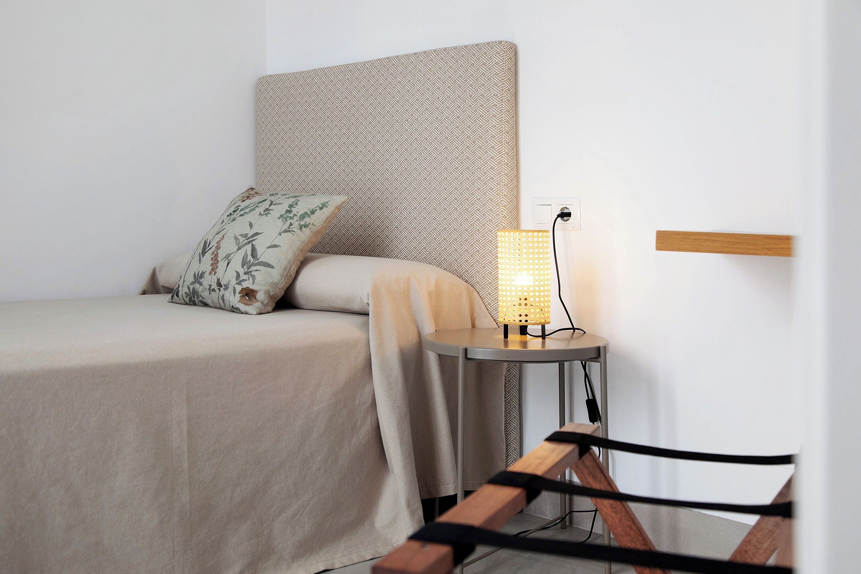 A neatly made bed with a patterned headboard, a bedside lamp, and a wooden bench.