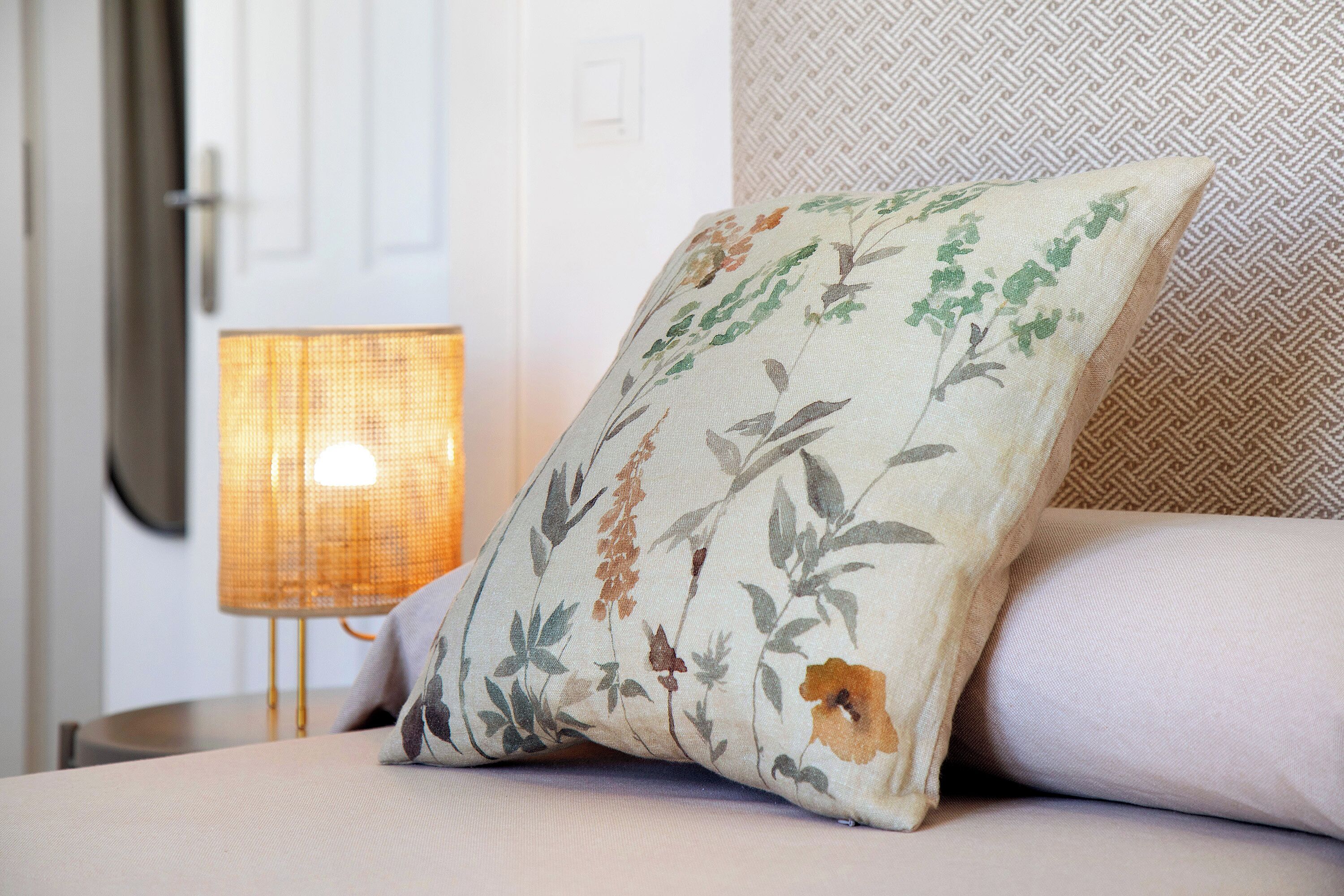 Een bed met een bloemenkussen, een lamp en een behang met patroon.