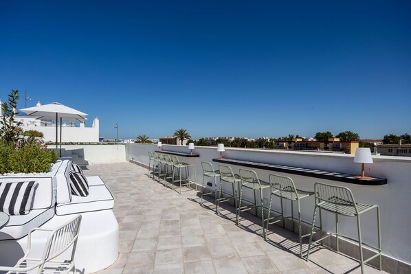 A rooftop terrace with a white outdoor seating area, including a sofa and chairs, and a grill.