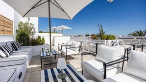 Une terrasse sur le toit, aménagée avec des meubles d’extérieur blancs, notamment des canapés et des tables, et protégée par de grands parasols.