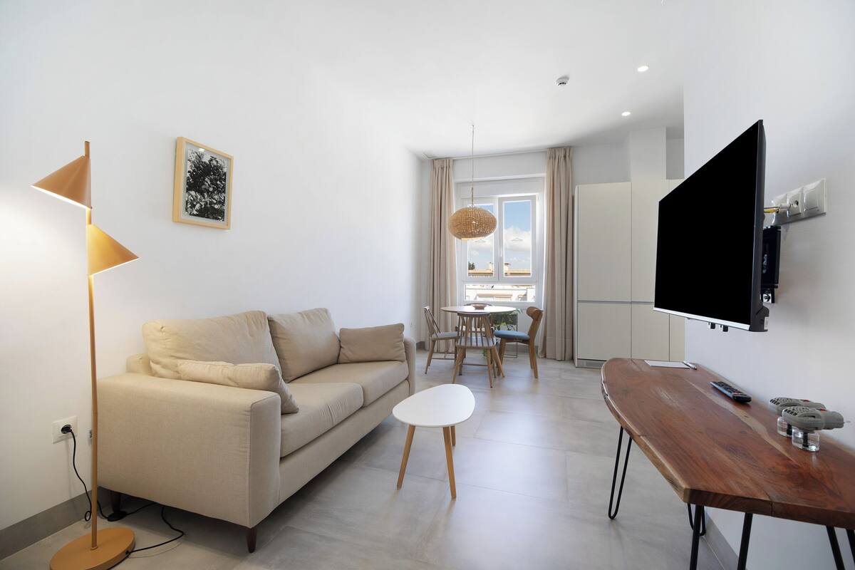 A modern living room with a sofa, a coffee table, a TV, and a dining area with chairs and a table.
