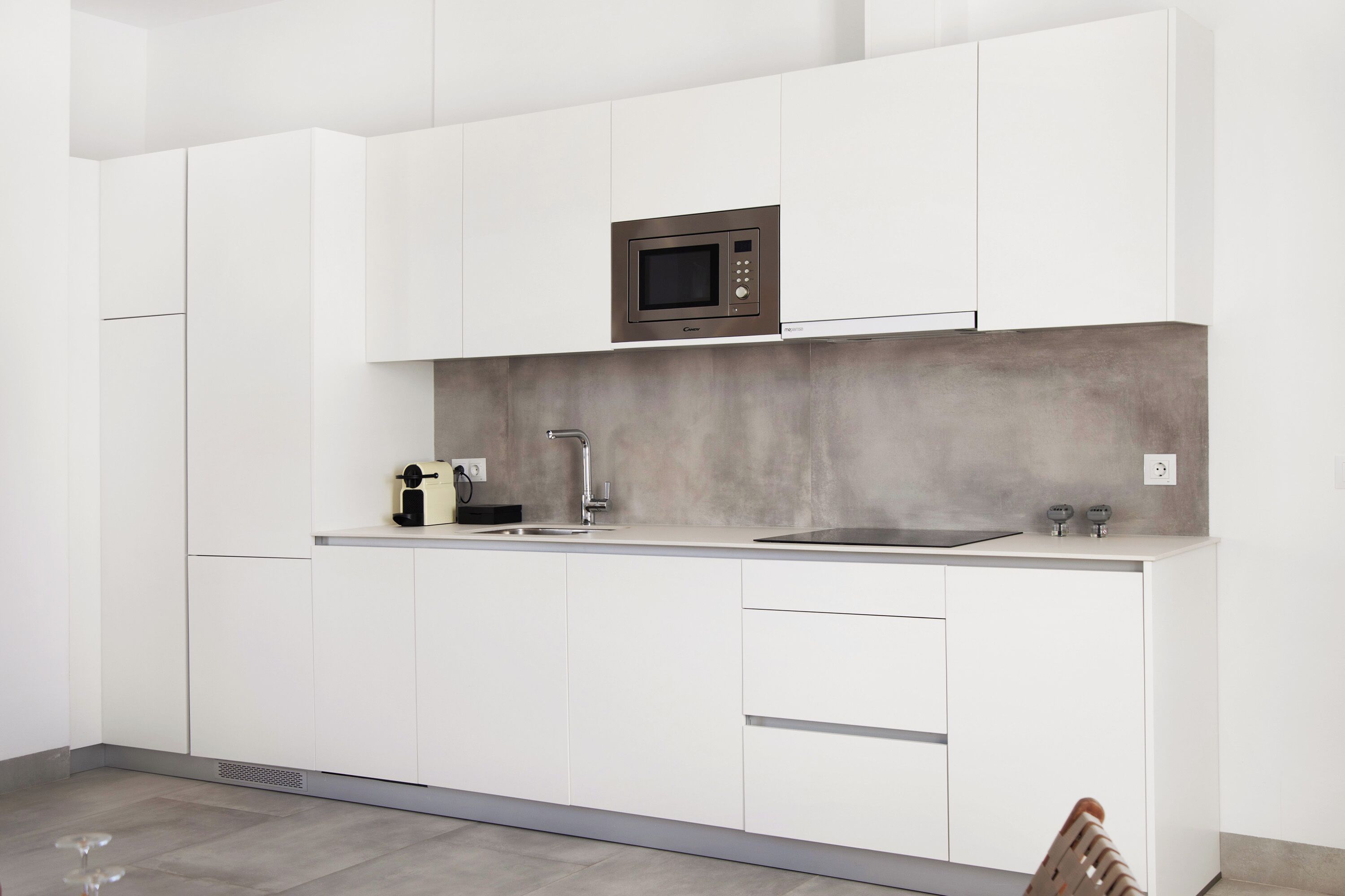 Een moderne keuken met witte kasten, een ingebouwde magnetron en een grijze achterwand.