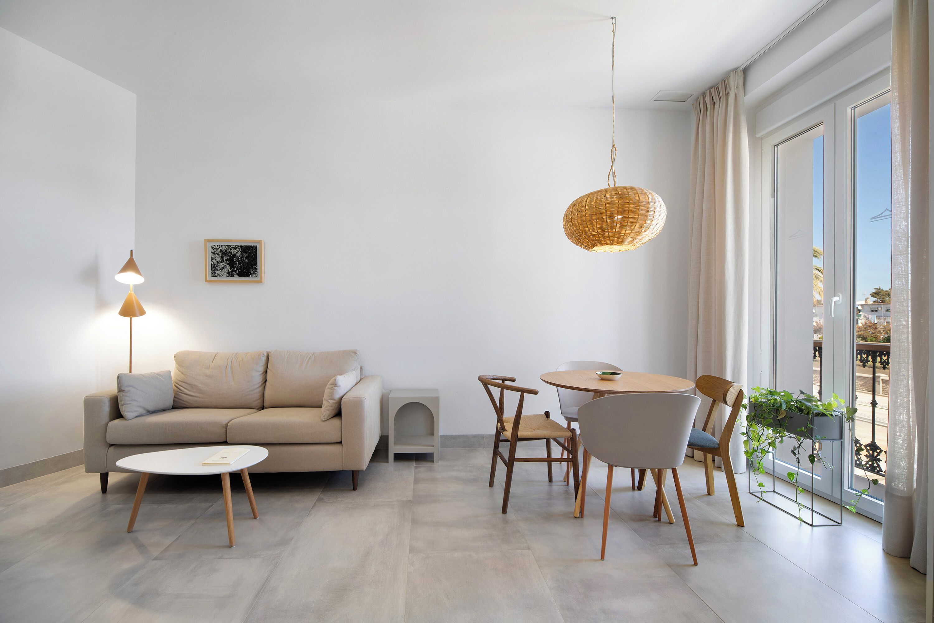 Ein modernes Wohnzimmer mit einer Couch, einem Couchtisch und einem Esstisch mit Stühlen. Eine Pendelleuchte und ein Fenster mit Vorhängen sind ebenfalls vorhanden.