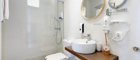 A modern bathroom with a glass-enclosed shower, a white toilet, a wooden vanity with a round mirror, and a white sink.